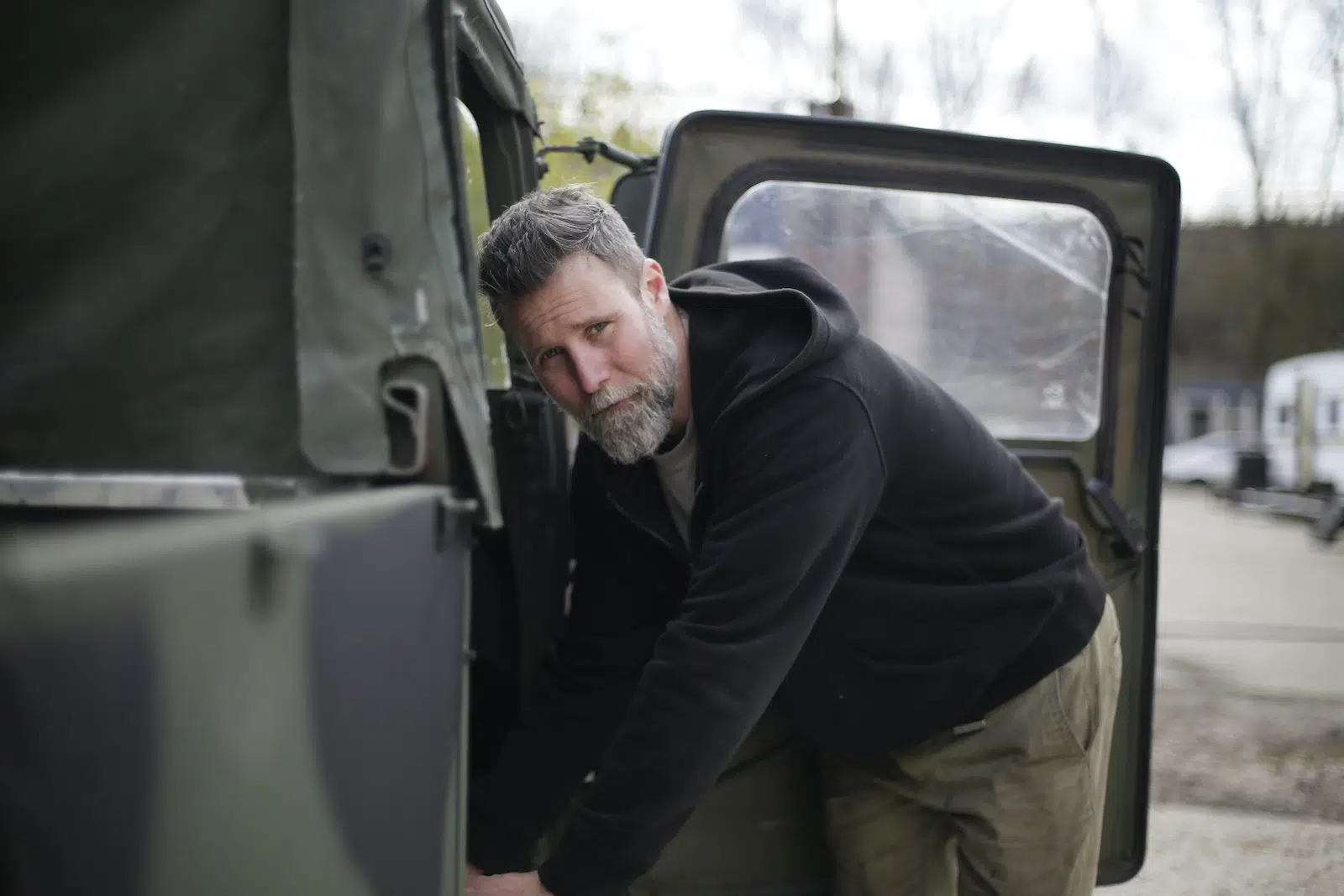 Bearded mechanic examining car on street near garage